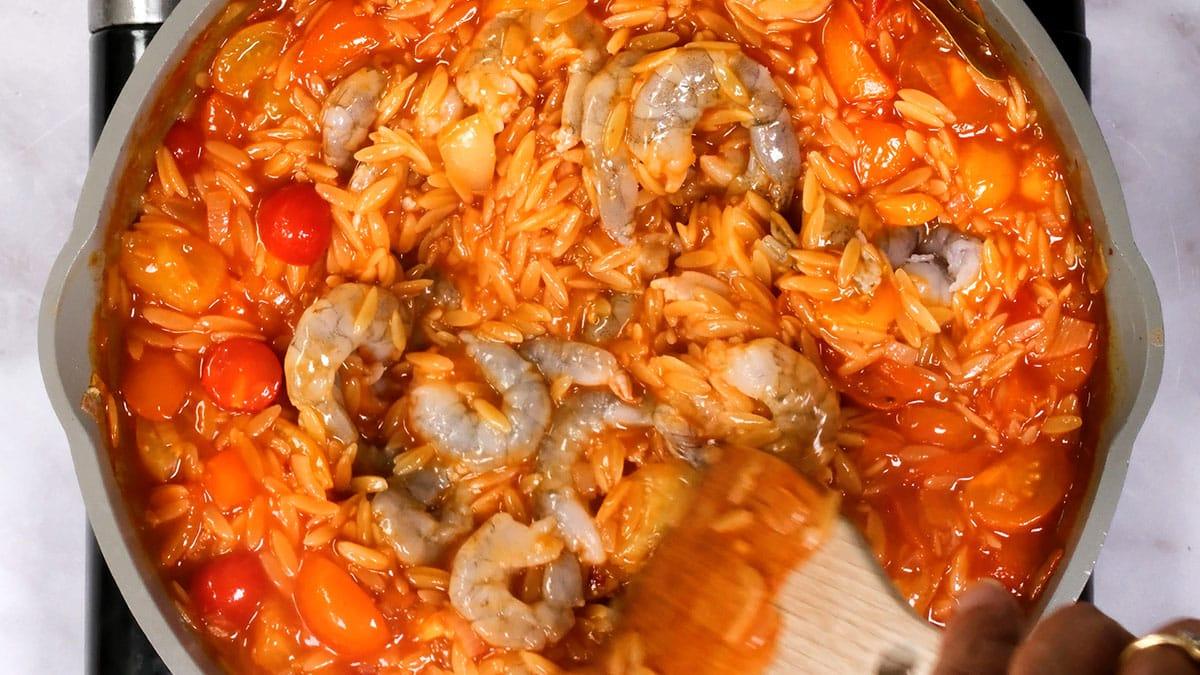 stirring raw shrimp into orzo pasta cooking with tomatoes