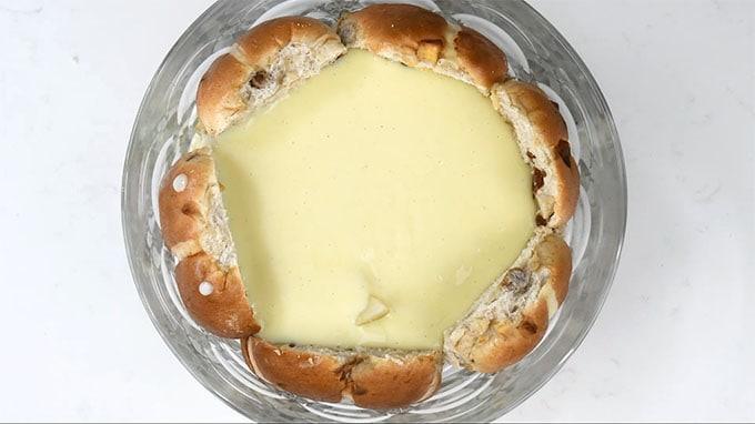 birds eye view of a trifle dish lined in sliced hot cross buns topped with sliced pears and custard