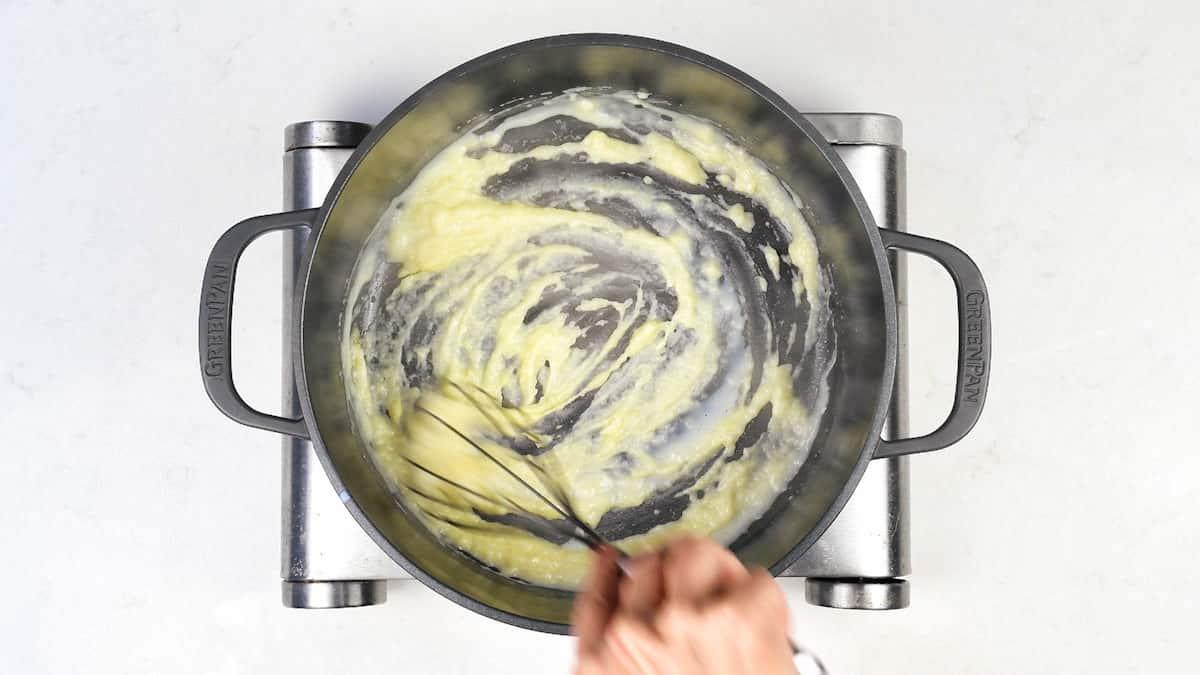 adding milk to roux in a pot to make a cheese sauce