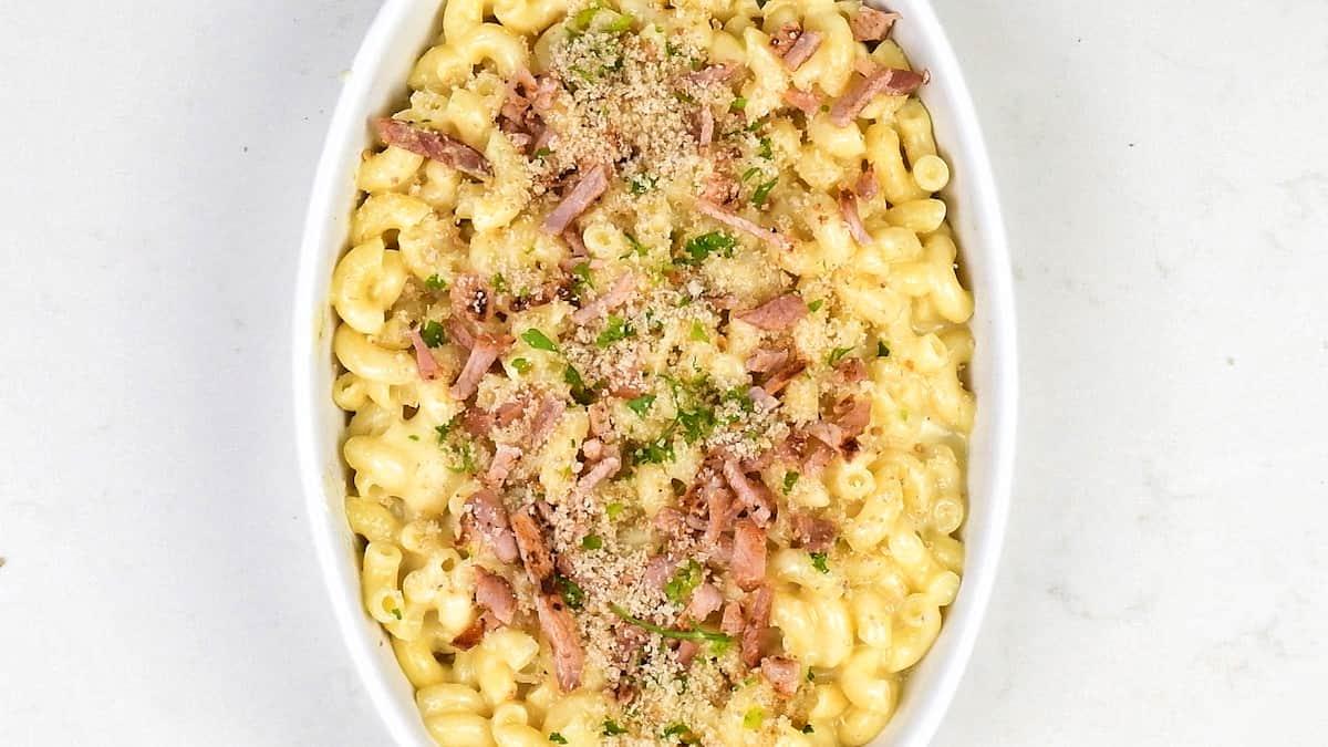 macaroni and cheese in a ceramic dish topped with breadcrumbs and bacon