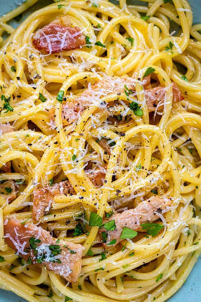 A close-up of authentic Carbonara, topped with grated cheese, crispy bacon, parsley, and black pepper. The creamy sauce coats the pasta perfectly, making this dish look freshly prepared and true to a traditional Carbonara recipe.