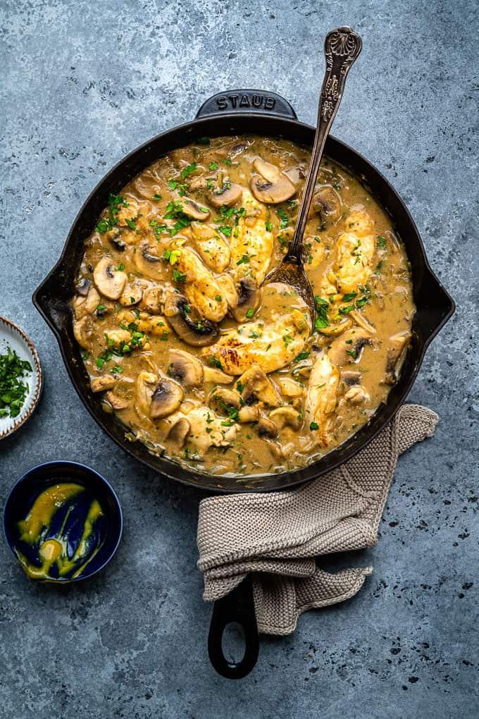 Skillet of slimming-friendly chicken stroganoff with mushrooms and parsley on a blue-grey background