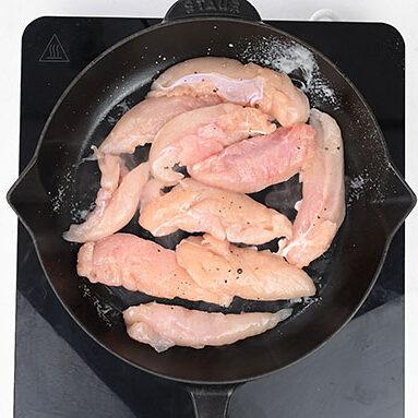 Seasoned raw chicken tenders in a cast iron skillet