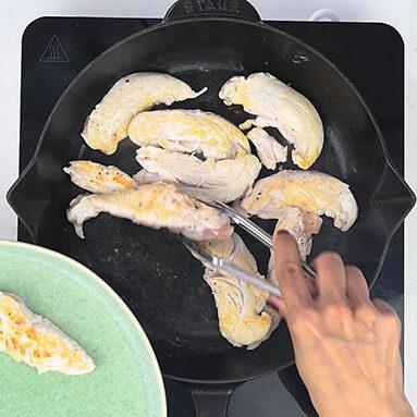 Turning browned chicken tenders in a skillet with tongs