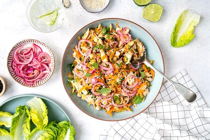 Close up of satay chicken salad with pickled onions, garnished with mint and sesame seeds