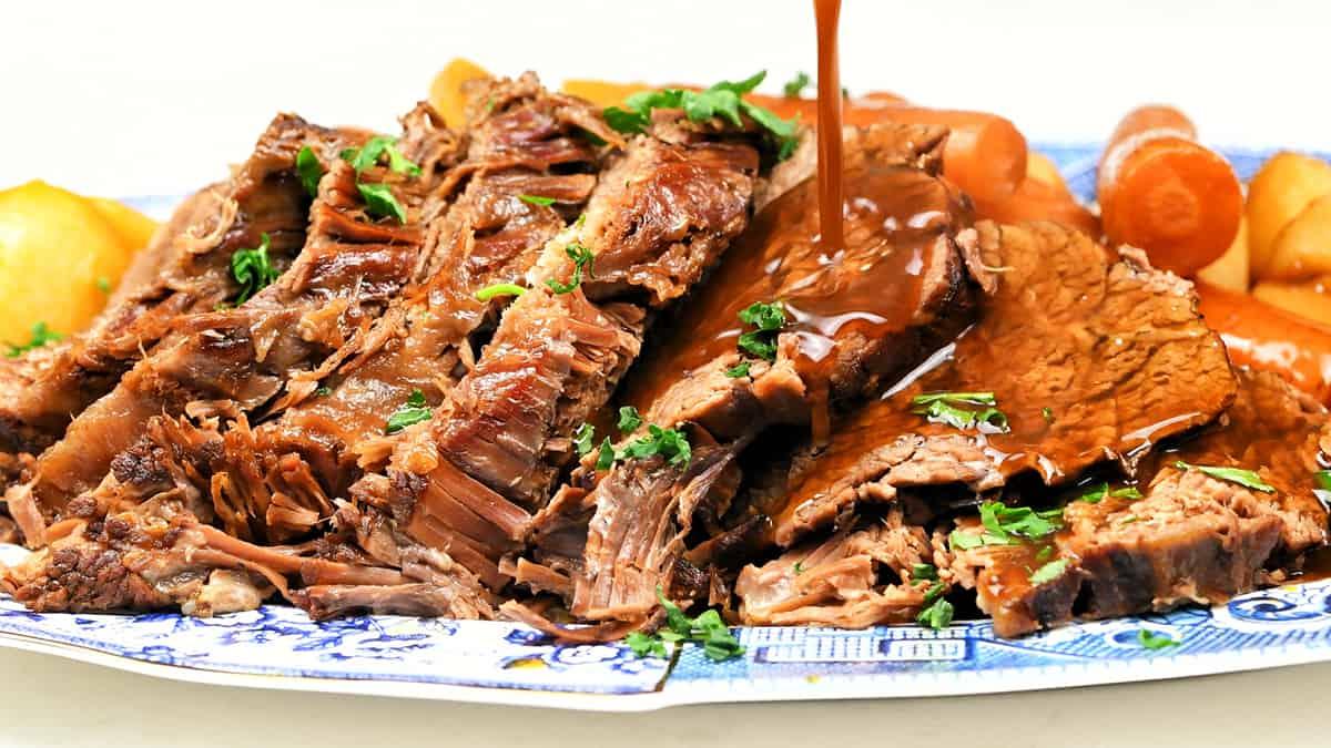 Close up on sliced roast beef with gravy being poured on