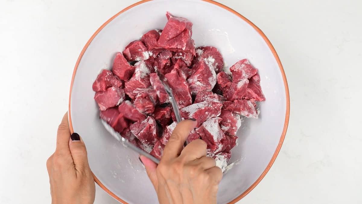 Tossing cubed beef with flour in a bowl