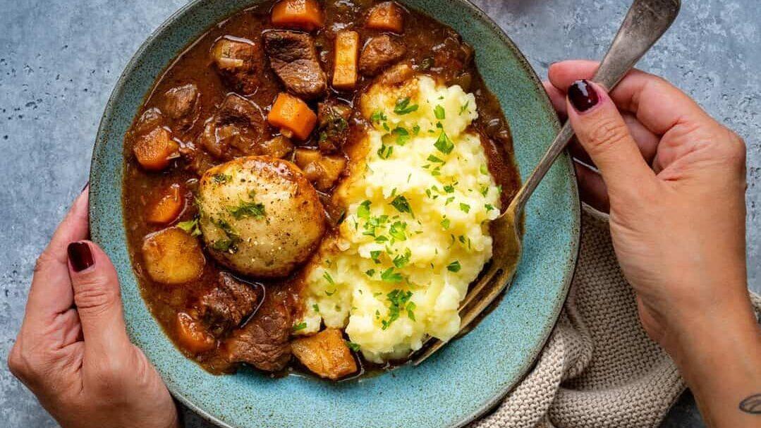serving of beef stew with dumplings and mashed potatoes in a blue bowl