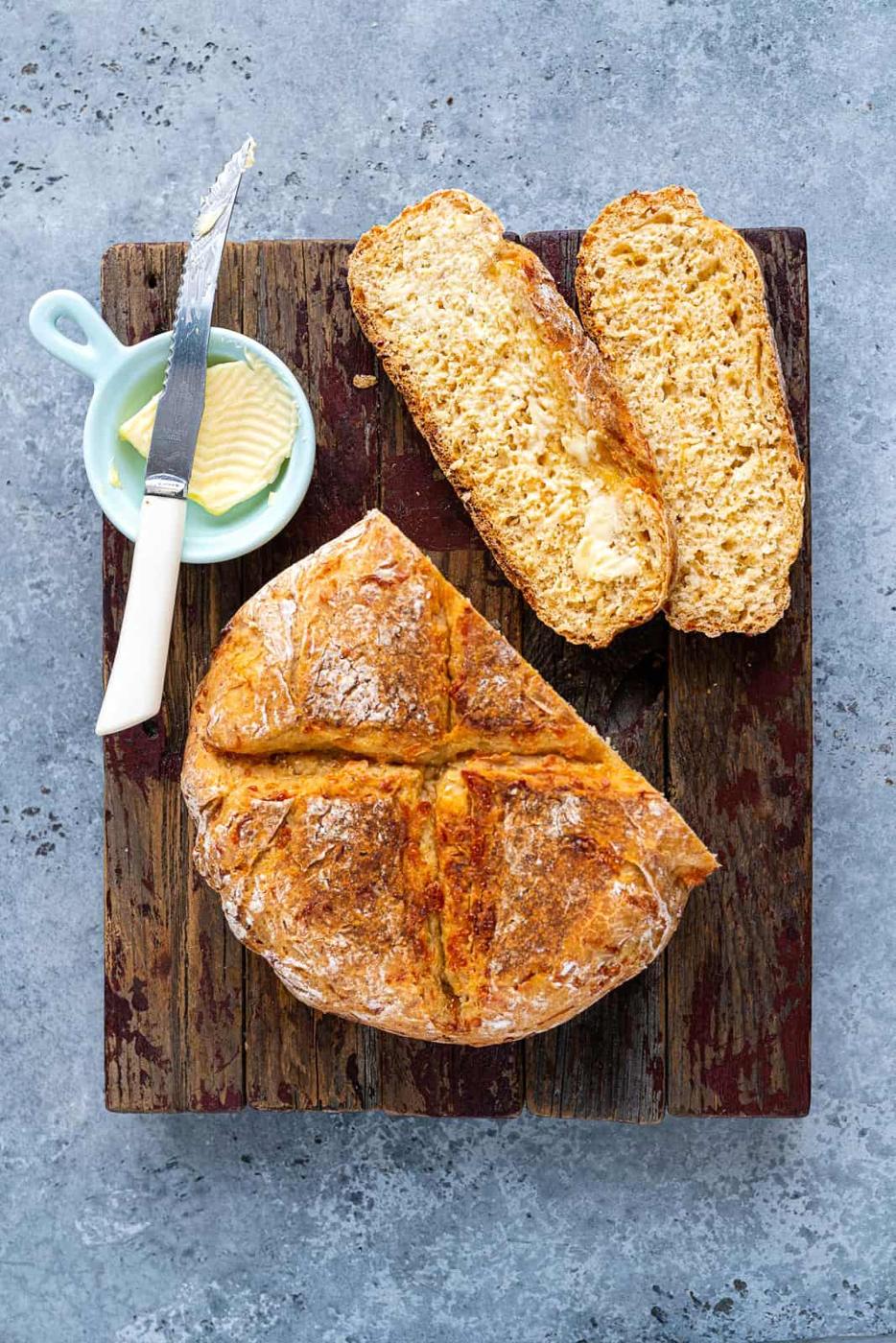 Slow Cooker bread with two slices cut out on a wooden board with butter on the side