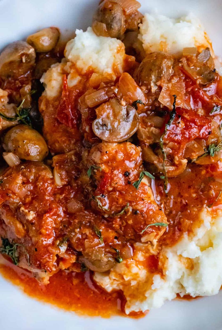 A close-up of Slow Cooker Chicken Chasseur with mushrooms and tomato sauce, served over creamy mashed potatoes on a white plate.