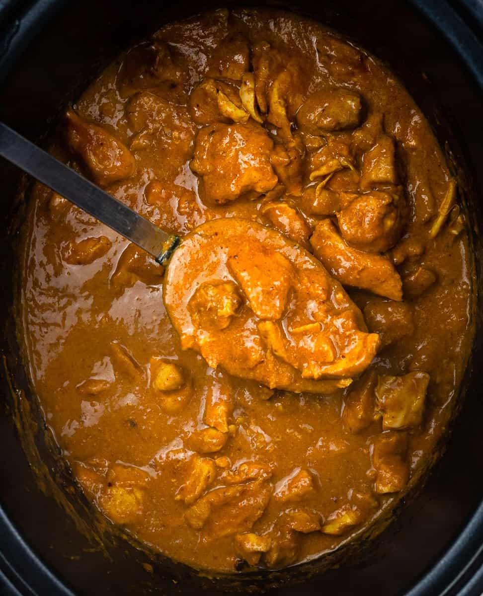 A close-up of a ladle scooping thick, orange-brown Slow Cooker Chicken Curry with chunks of chicken from a slow cooker—an easy curry recipe perfect for cozy nights.