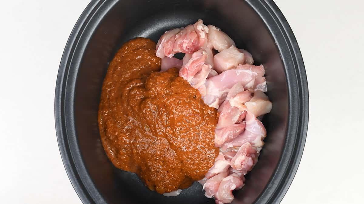 Raw, diced chicken pieces and a thick, brownish-orange sauce sit side by side in a black slow cooker, ready to become a flavorful Slow Cooker Chicken Curry—an easy curry recipe perfect for busy days.