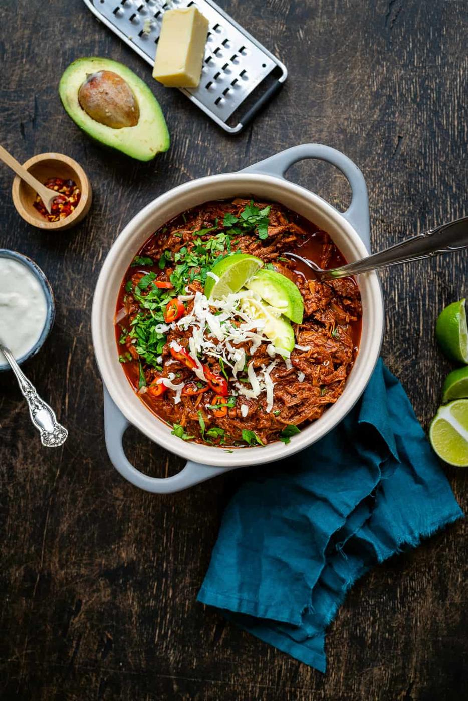 Pot of chunky beef chili topped with avocado, shredded cheese and cilantro