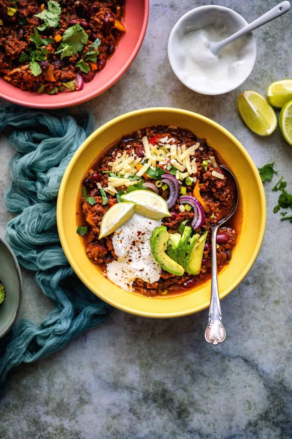 Bowl of chilli with sour cream on the side plus garnishes