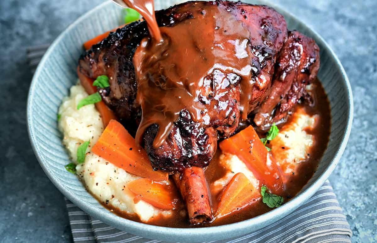 Slow cooker lamb shank served over mashed potatoes and carrots drizzled with red wine gravy