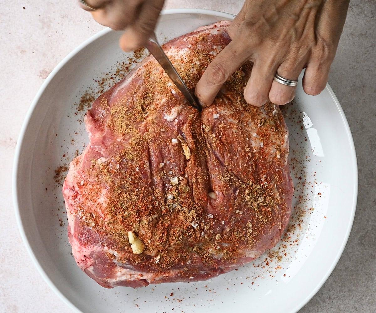 stuffing garlic cloves into seasoned shoulder of lamb