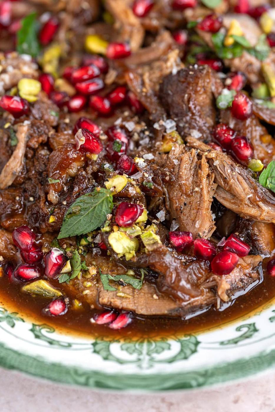 close up on slow cooked lamb garnished with pomegranate seeds and mint leaves