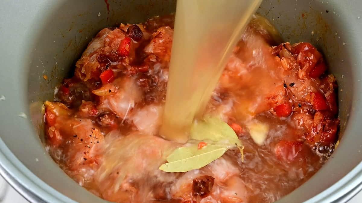 Adding stock to slow cooker containing paella ingredients