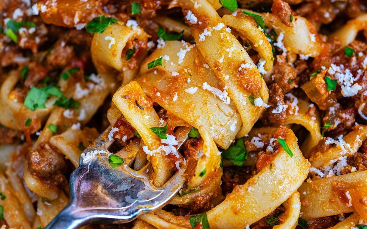 Close up on bowl of tagliatelle with Italian ragu sauce, grated Parmesan and chopped parsley