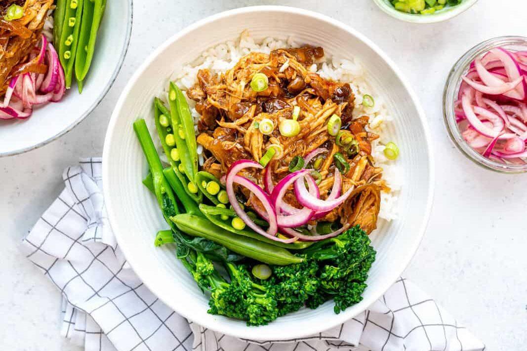 Teriyaki chicken served in white bowl over rice with steam broccoli and sugar snap peas