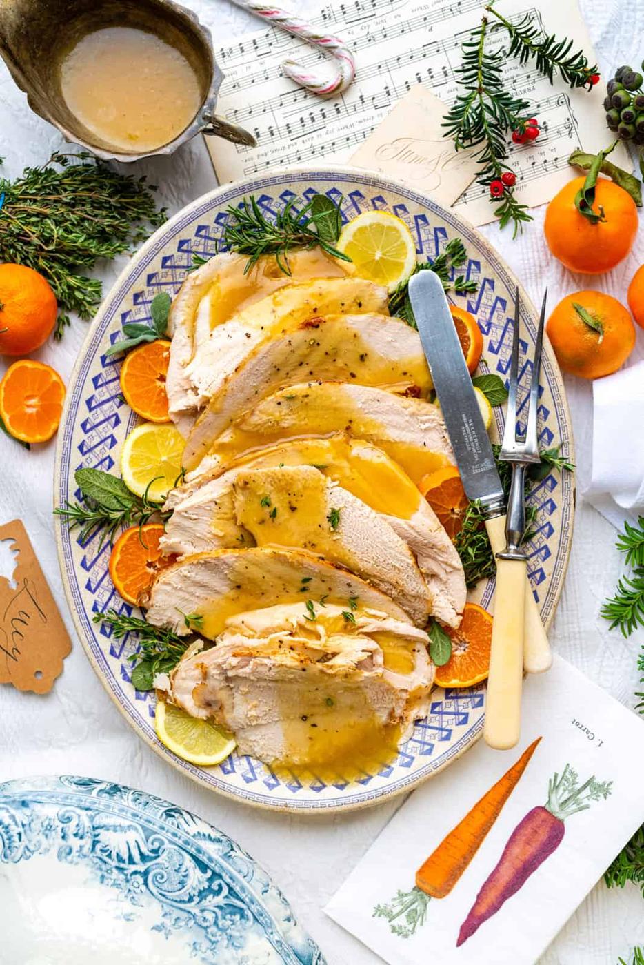 Slow Cooker Turkey breast sliced and arranged on a platter on a bed of herbs and citrus slices and drizzled with gravy