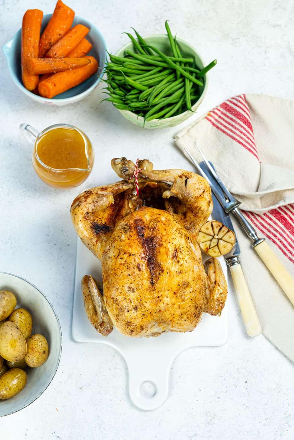 Whole roast chicken on a small ceramic white board with gravy on the side