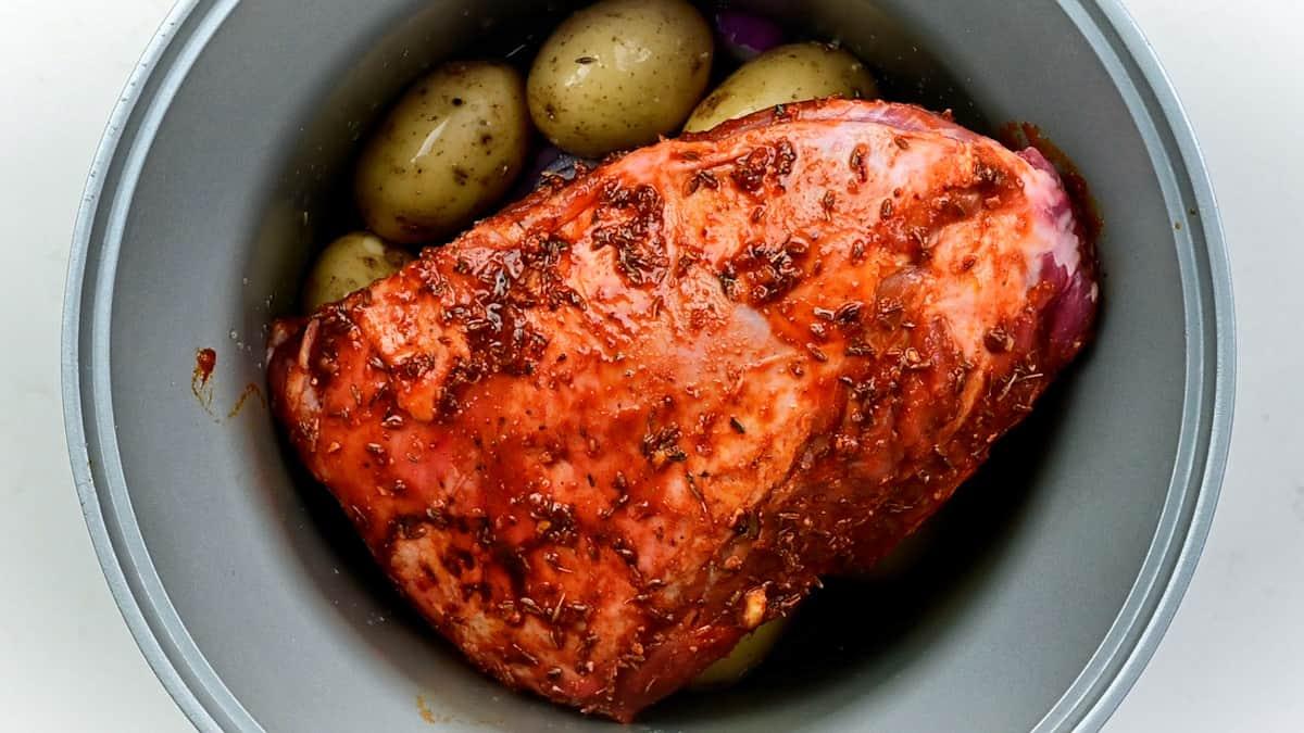 Marinated half shoulder of lamb positioned over otatoes, onions and stock in a slow cooker