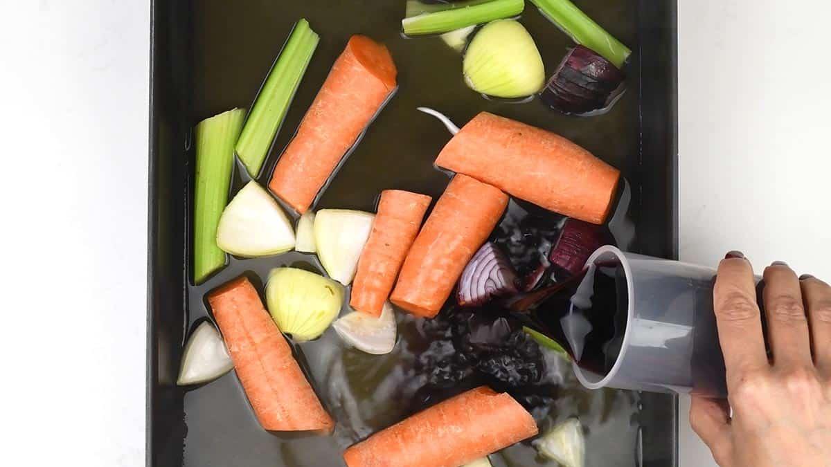 chopped vegetables in a deep-sided roasting tin with wine and stock
