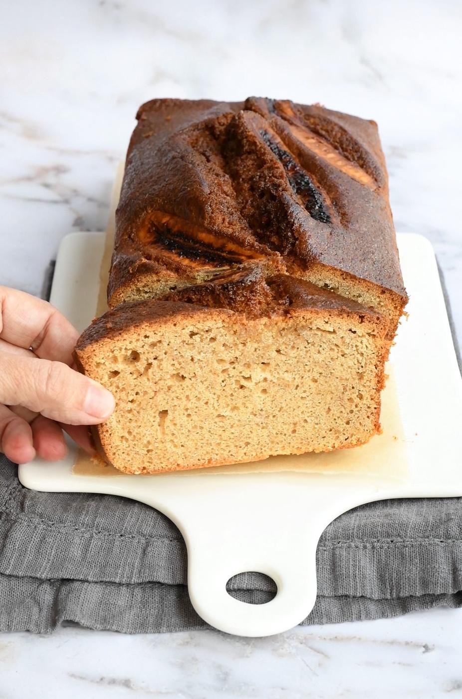 Banana bread made with sourdough discard, one slice cut at an angle with hand holding it
