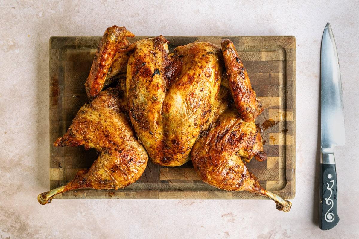 roast spatchcock turkey on a wooden board, large carving knife on the side