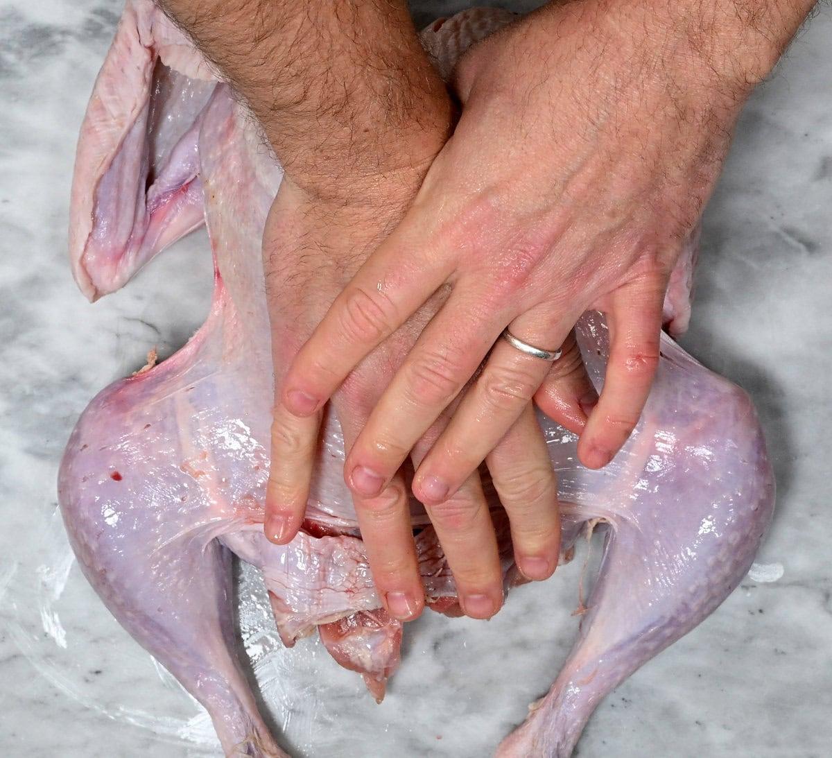 pressing a spatchcock turkey flat with palms of hand to flatten