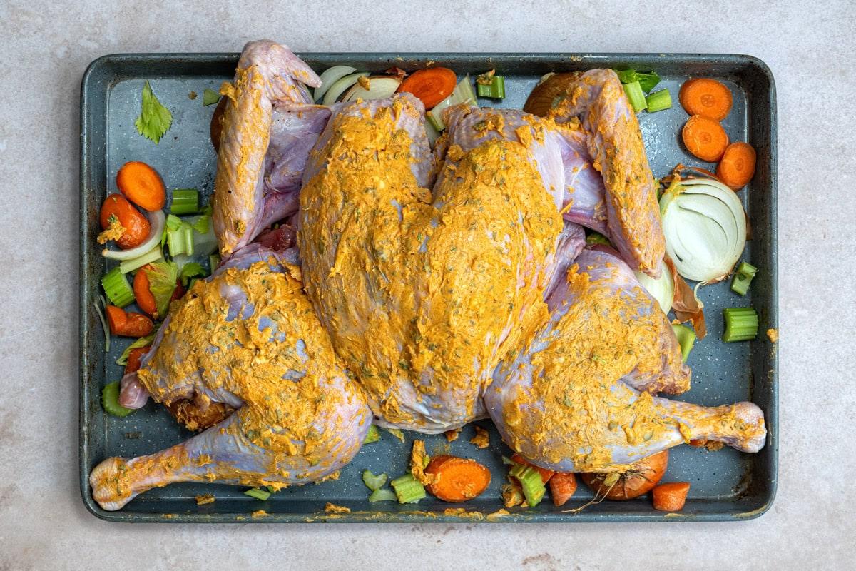 butterflied whole turkey on a bed of vegetables in a roasting pan
