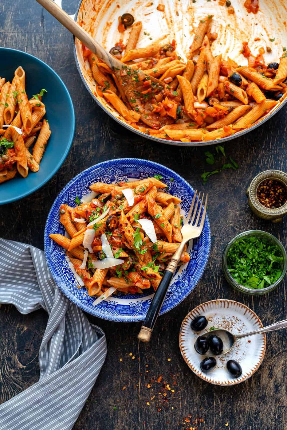 Bowl of pasta puttanesca with shavings of Parmesan and chopped parsley