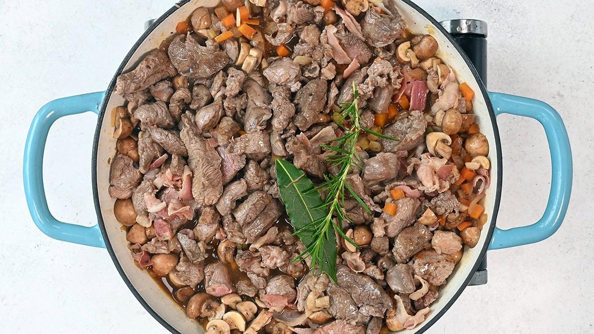 beef stew ingredients topped with bay leaf and rosemary