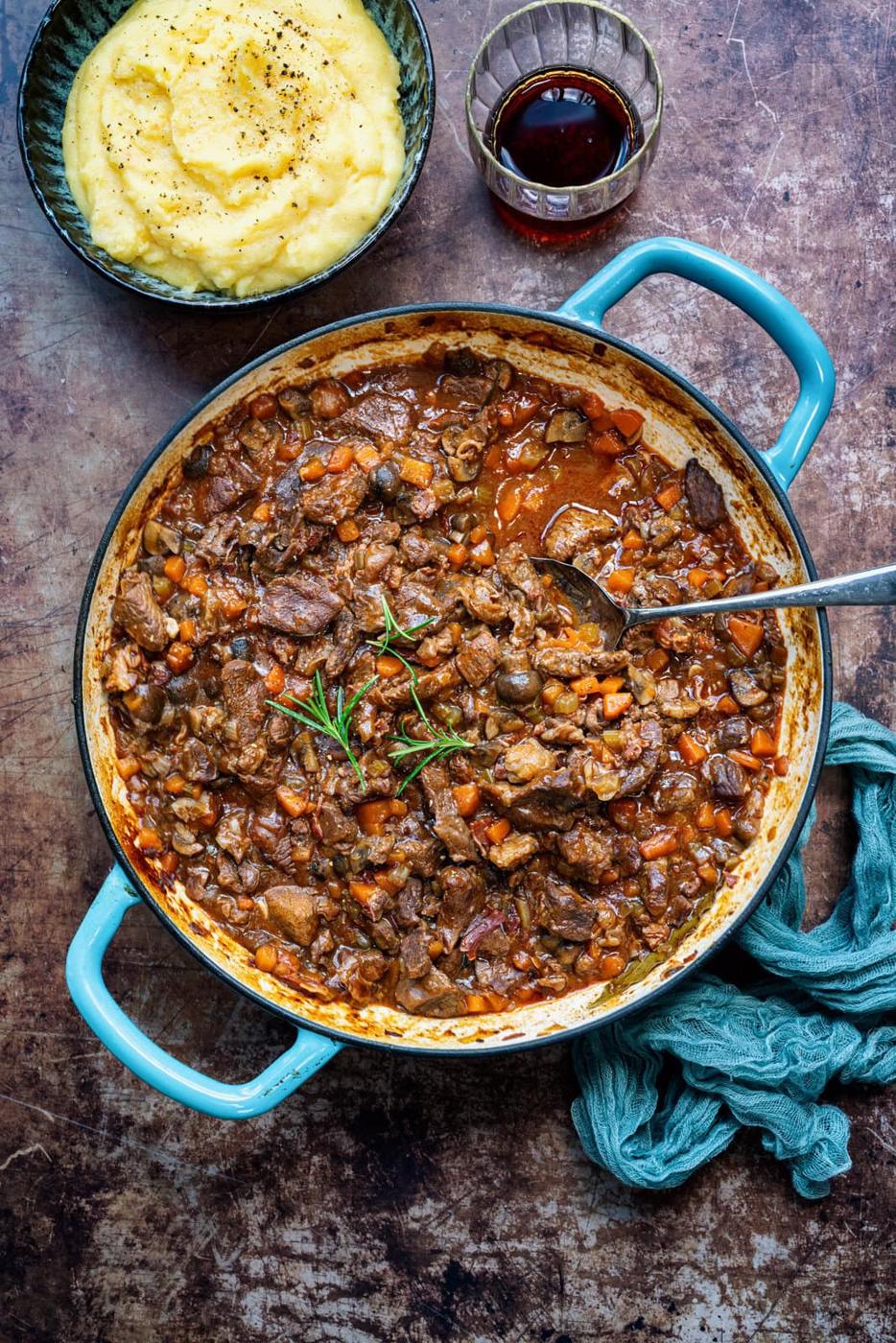 cast iron casserole with Italian beef stew, bowl of polenta and glass of red wine on the side