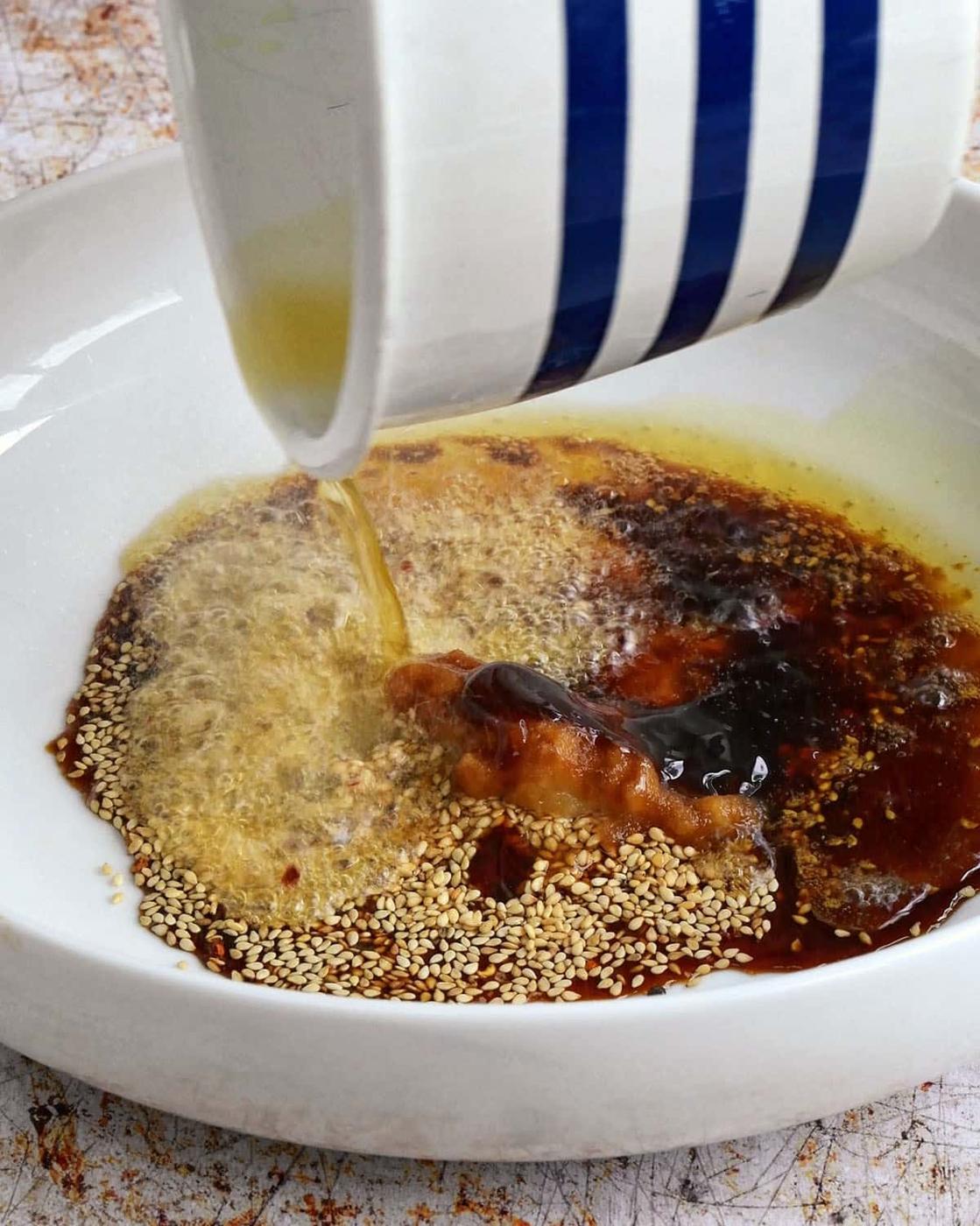 adding hot oil to bowl of ingredients for spicy ramen