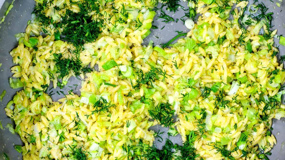 cooking orzo with vegetables and dill in a pan