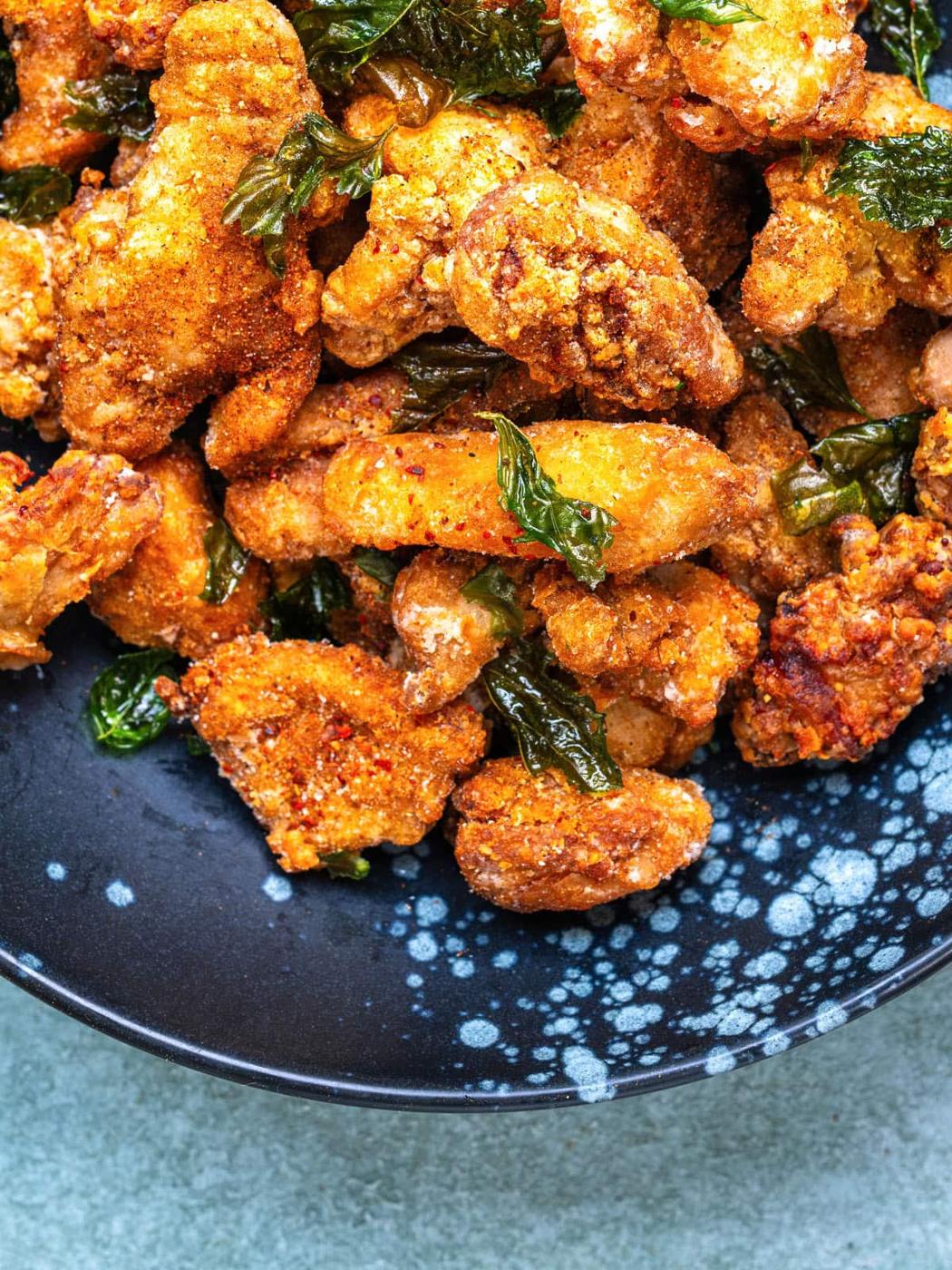 Crispy Taiwanese fried chicken pieces tossed with fried Thai basil on a dark blue speckled plate