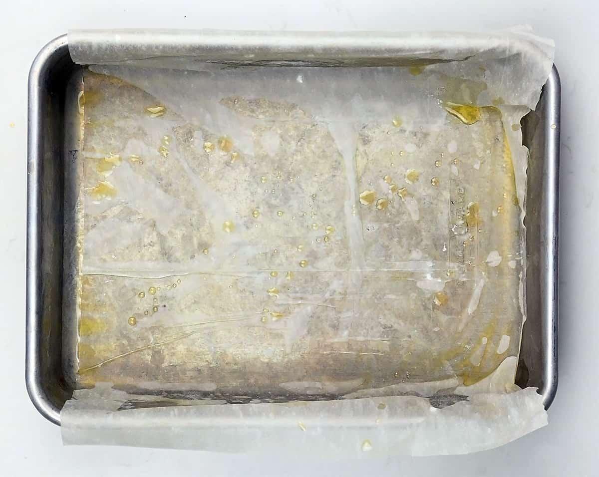 A metal baking pan lined with parchment paper and lightly greased, ideal for preparing Greek cheese pie like Tiropita with its signature crisp phyllo pastry, sits on a white surface.