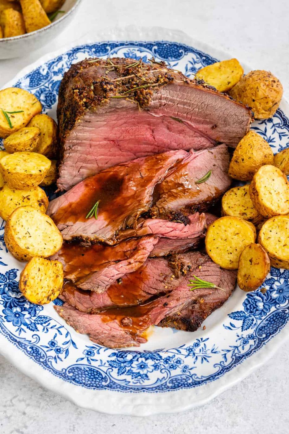 Sliced roast beef and gravy on a platter with roast potatoes