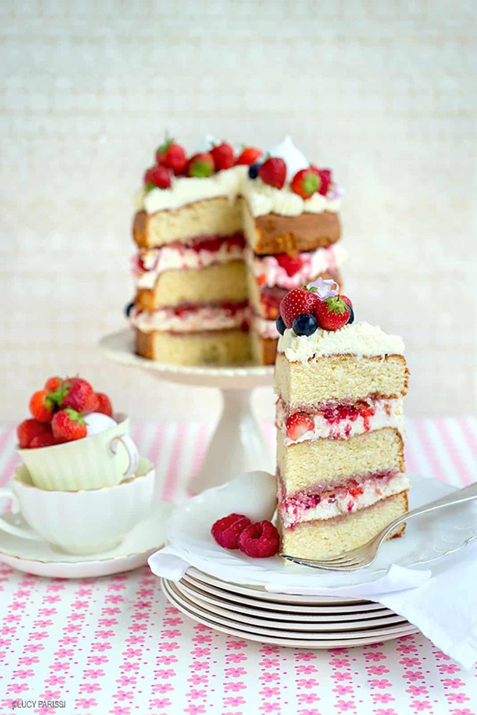 Slice of tall layered mixed berry eton mess cake with strawberries, raspberries and blueberries on a pretty flower patterned background
