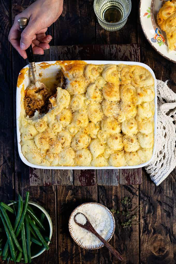 Traditional Shepherd’s Pie topped with mashed potato in a ceramic dish with slice taken out