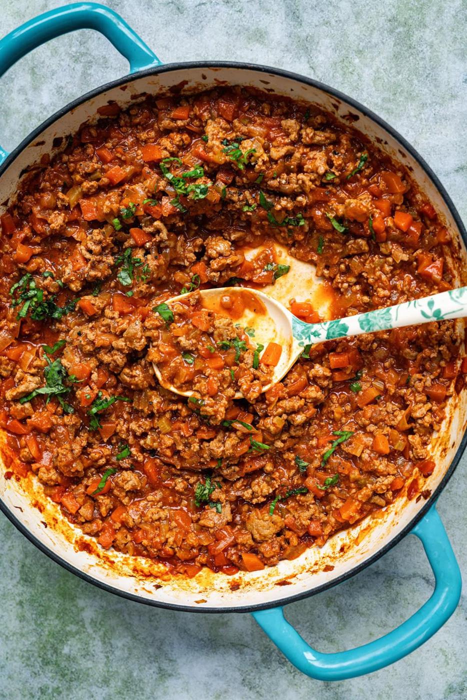 cast iron braiser with Turkey Bolognese sauce, large spoon resting in the sauce