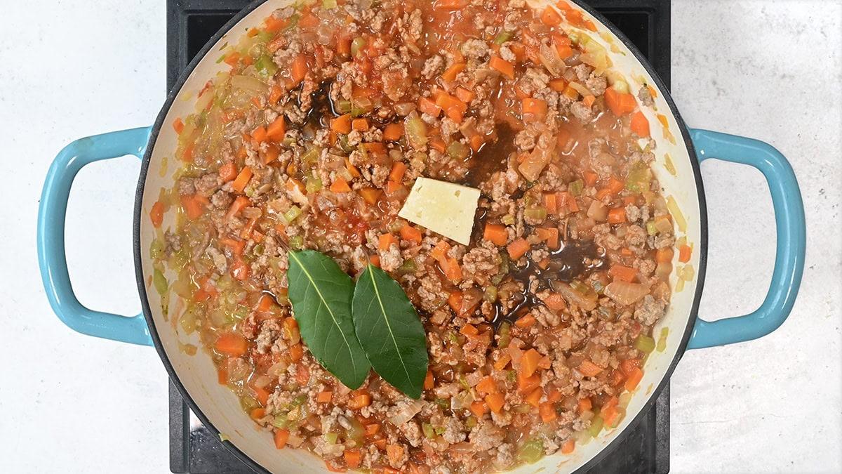 turkey bolognese with a piece of cheese rind and bay leaves in a cast iron braiser