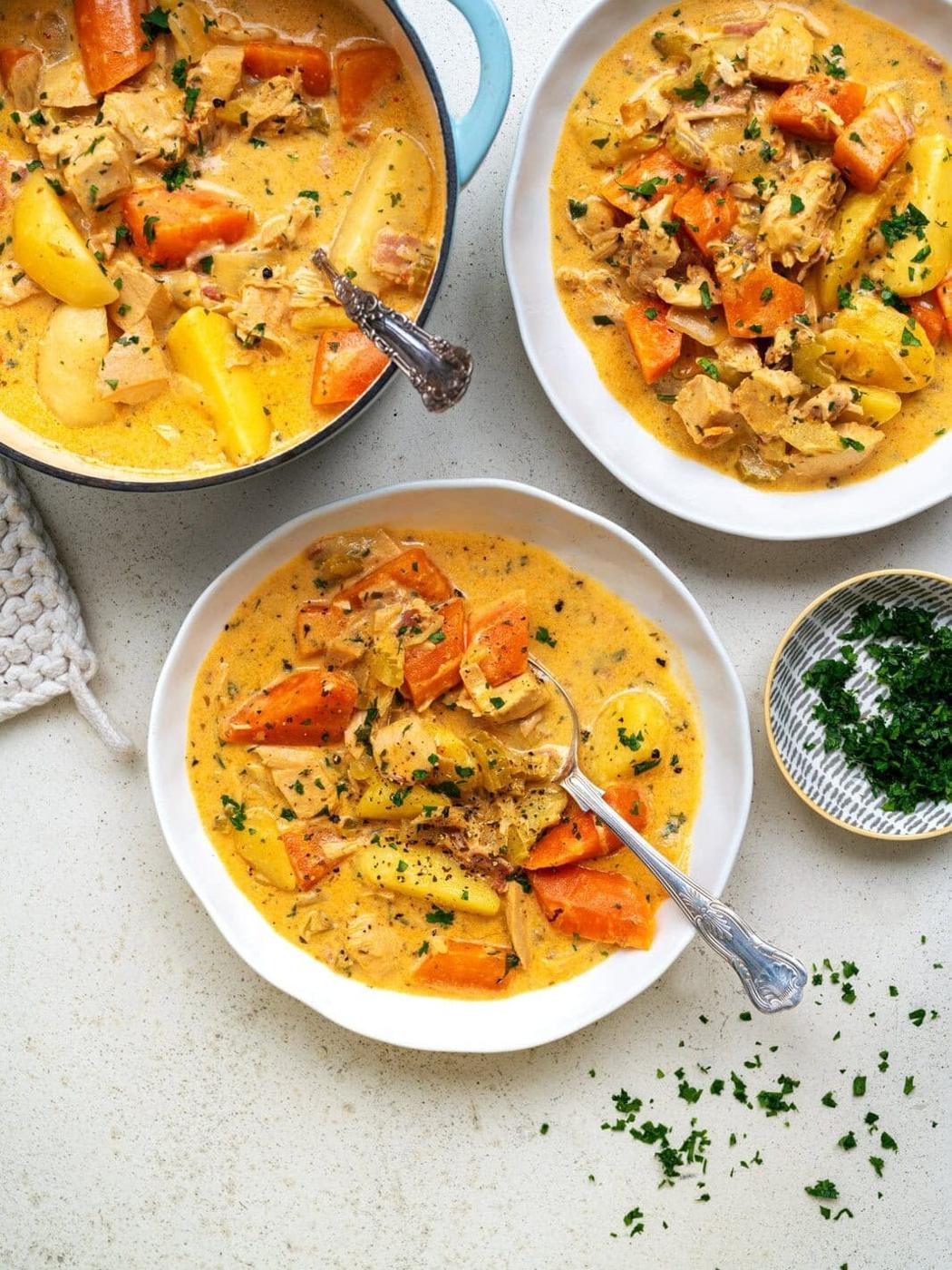 Two large bowls of turkey stew with a cast iron pot on the side, bird's eye view