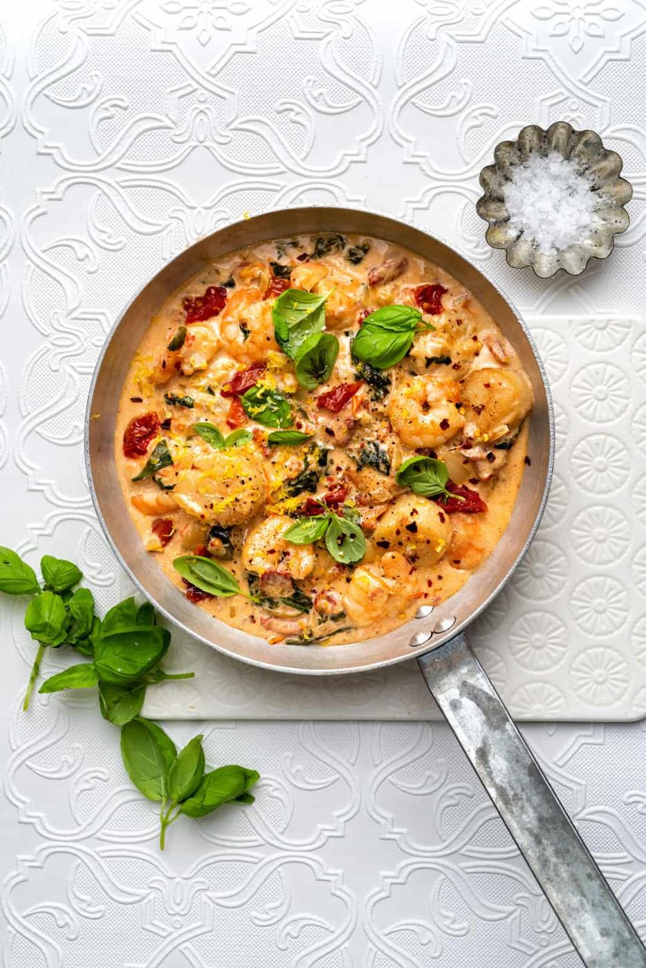 Pan with shrimp and scallops cooked in a creamy sauce with basil leaves on the side