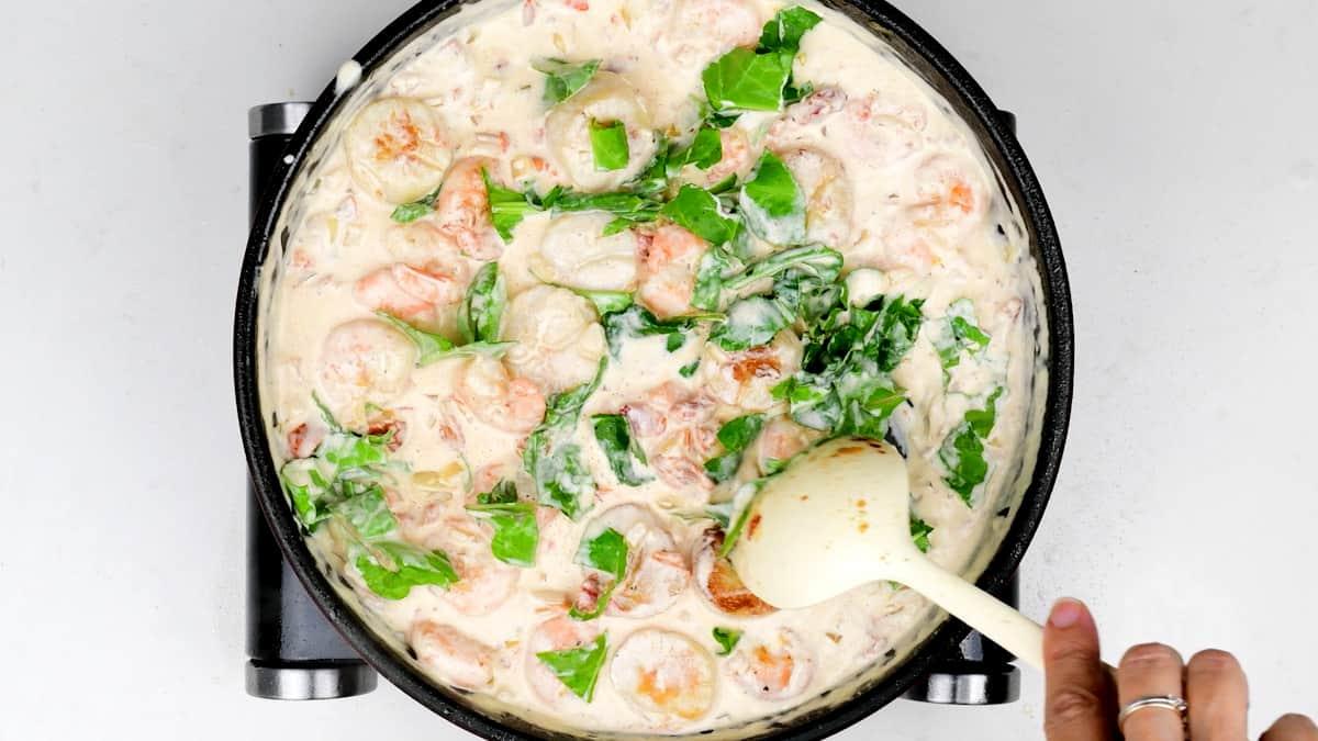 stirring spinach into creamy Tuscan sauce