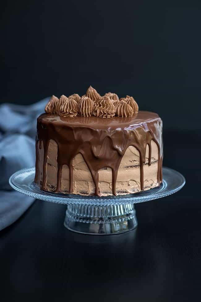 Chocolate layer cake with Nutella filling and frosting and chocolate glaze on a glass cake stand