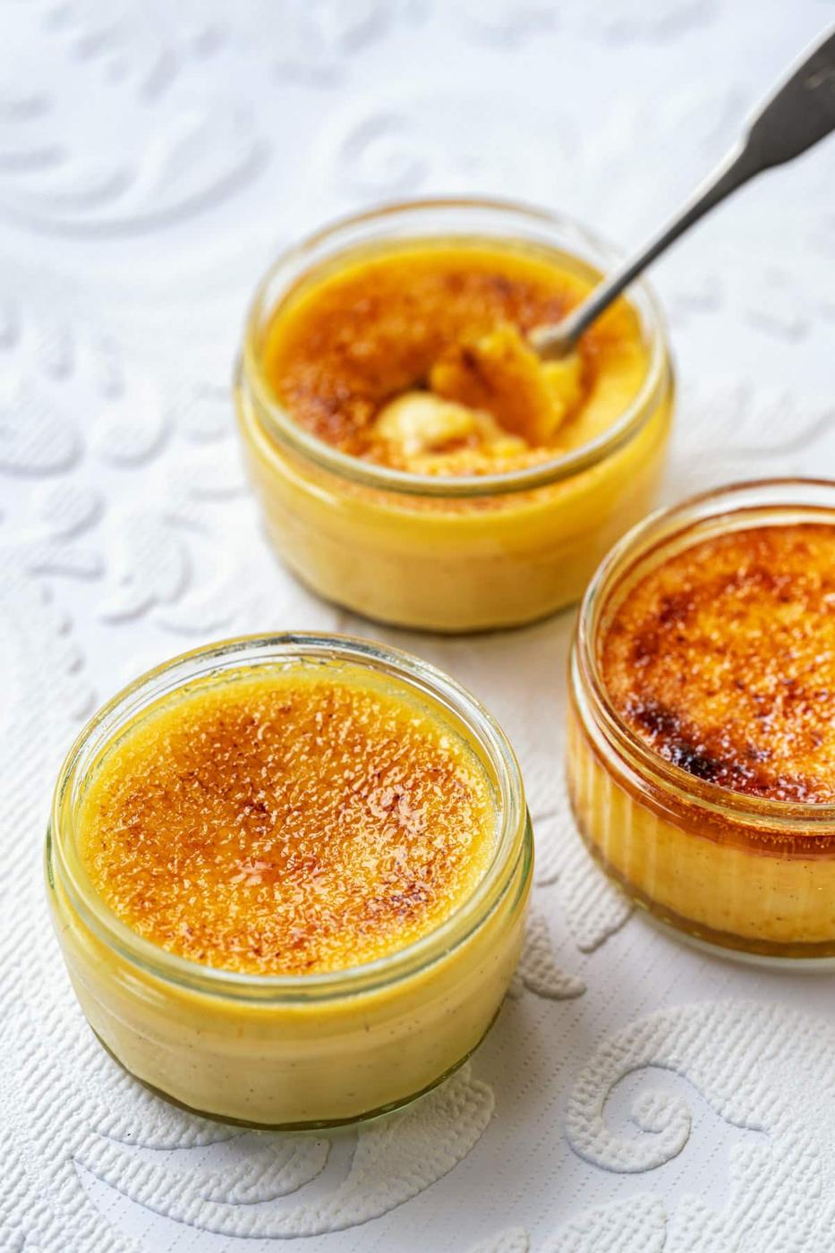 Three glass ramekins of Creme Brulee, one with a spoon in it