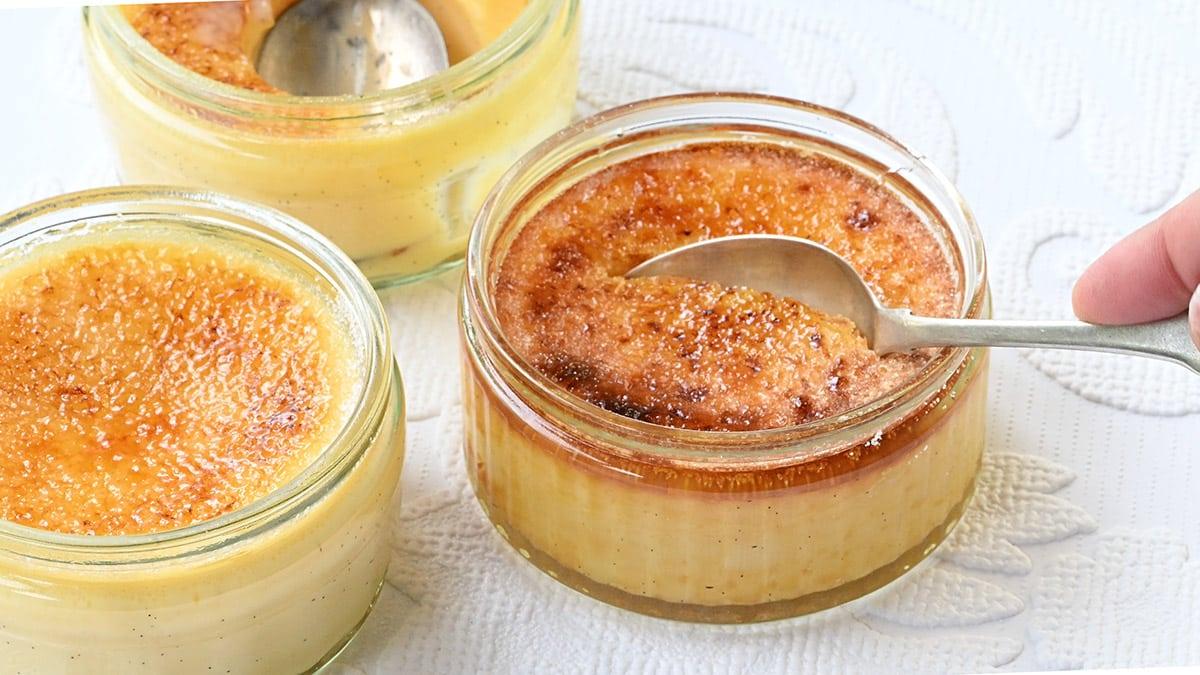 Close up on creme brulee ramekins, one with a spoon breaking through sugar crust